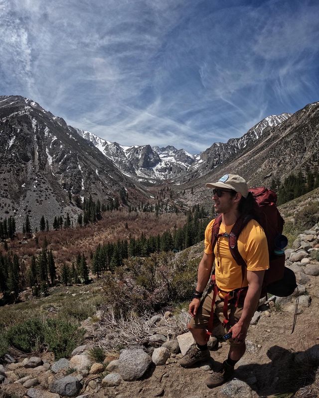 Wil Dasovich in a yellow t-shirt and light pale brown shorts in a rocky place.